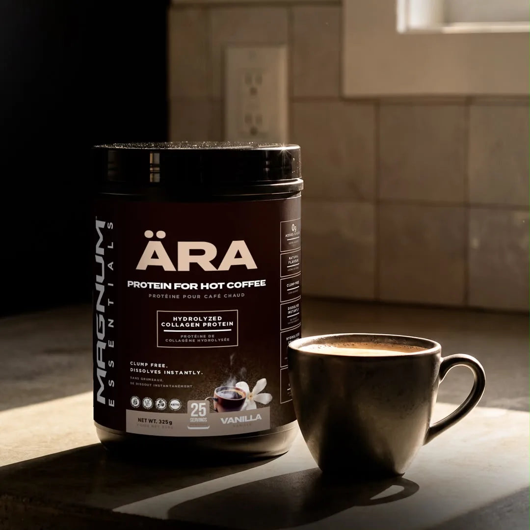 A tub of ÄRA Vanilla protein for hot coffee beside a dark mug of coffee on a sunlit counter